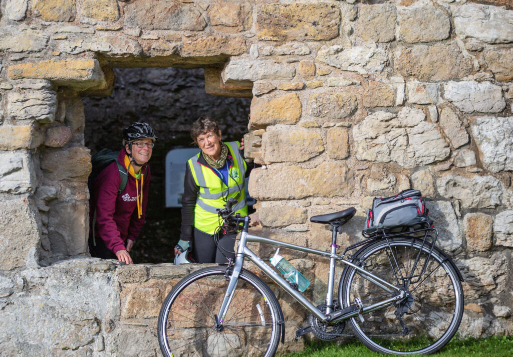 Cyclists look through a window at Penmon Priory during a guided cycle ride on Anglesey